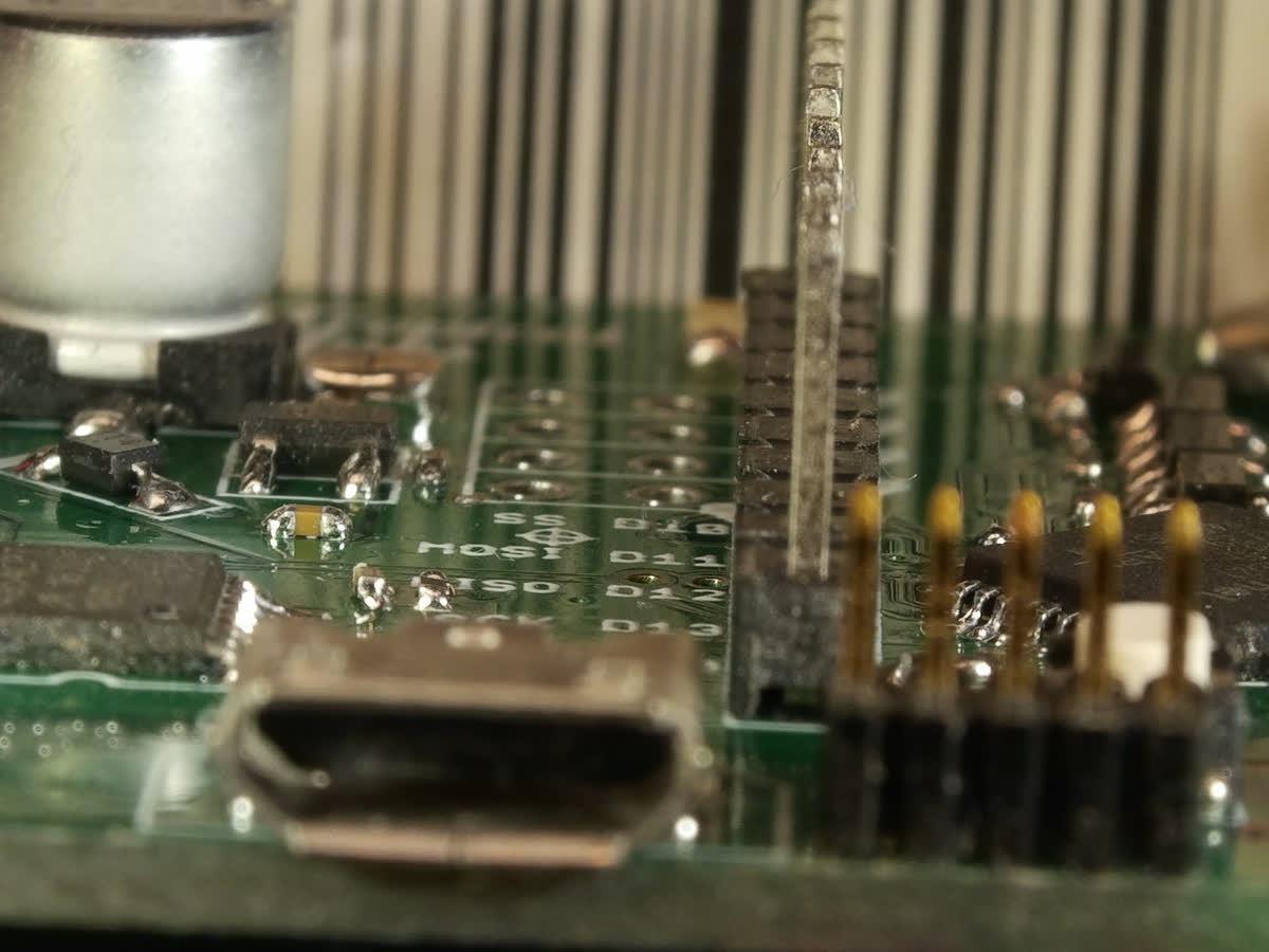 One frame of a seven-frame focus bracket of a circuit board: the silkscreen and solder pads mid-board are sharp; the header pins in front, the USB socket and the capacitor are soft.